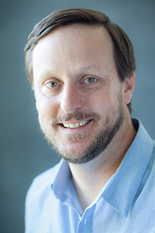 "portrait of a man with short brown hair, wide smile and blue collared shirt"